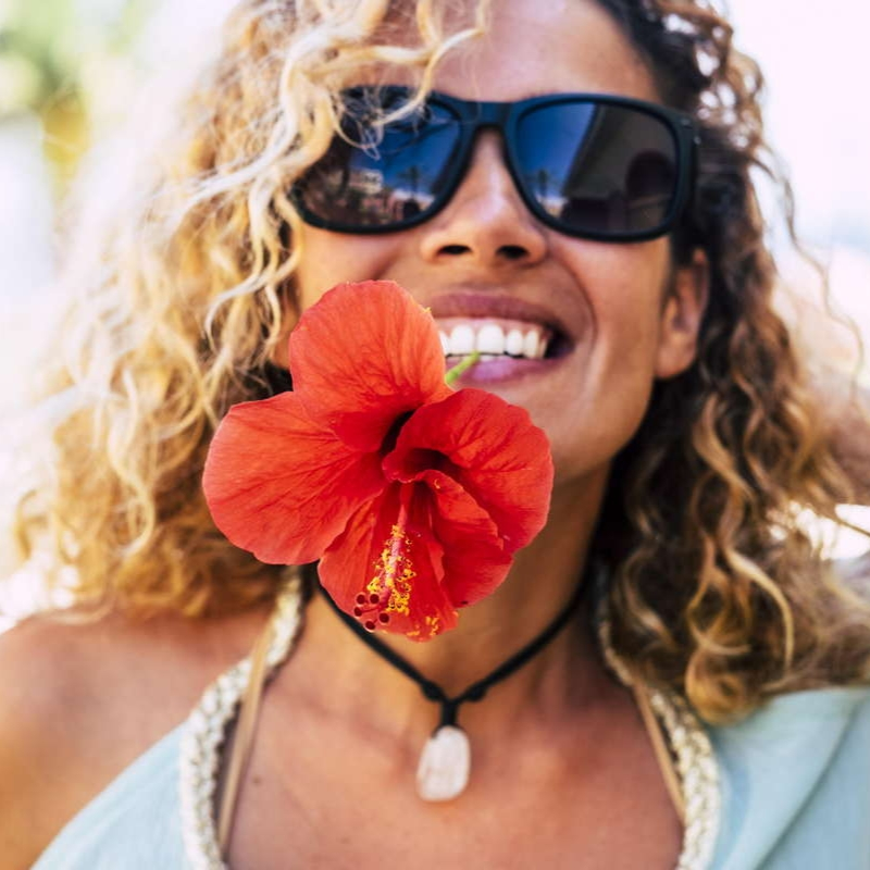 Foto de una mujer sonriendo con una flor en los dientes